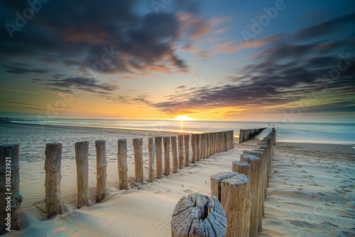 Groynes and wave breakers in a smooth sea just before sunset at a Dutch coast