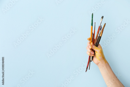 Hand of artist with brushes on color background