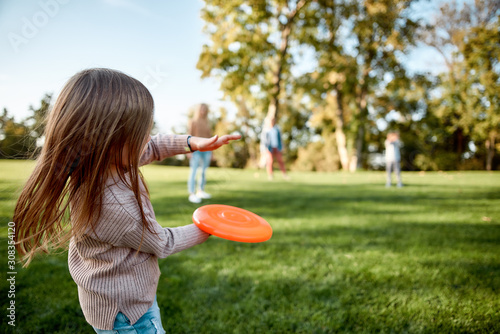 Making memories, breaking the distance. Little girl playing frisbee with her family in the park on a sunny day