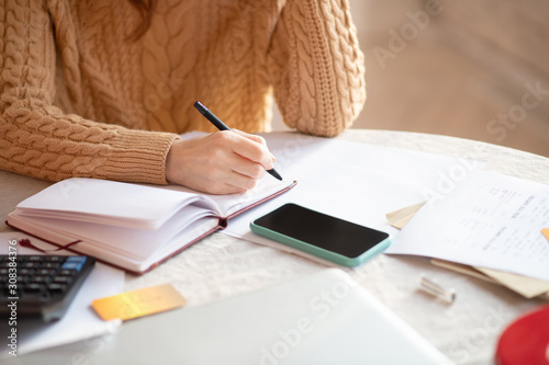 Dark-haired woman in knitted sweater writing in her notebook