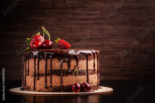 Chocolate cake with with berries, strawberries and cherries. cake on a dark brown background. copy space