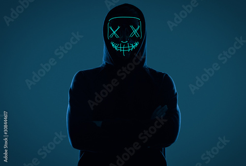 Anonymous man in black hoodie hiding his face behind a neon mask