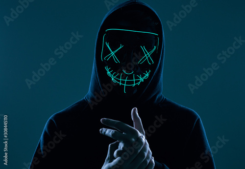 Anonymous man in black hoodie hiding his face behind a neon mask