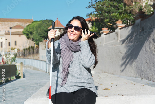 Blind woman with a white cane using a smartphone to listen some messages. Visually impaired concept with empty copy space.