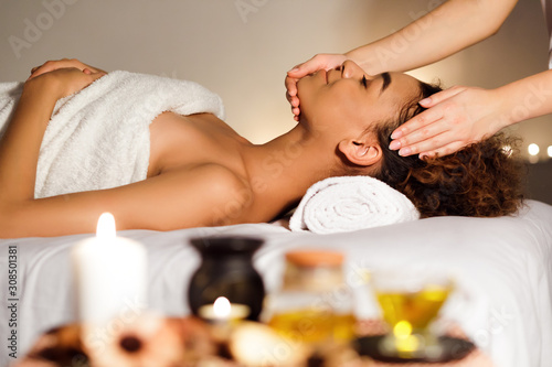 Afro girl receiving face massage with aroma composition nearby
