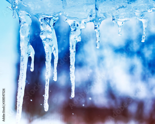 beautiful natural background with shiny transparent icicles hanging from the roof on a spring Sunny day