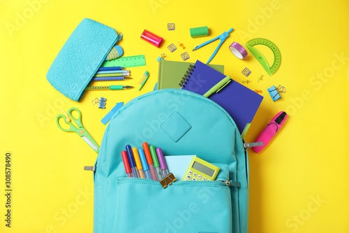 Stylish backpack with different school stationery on yellow background, flat lay