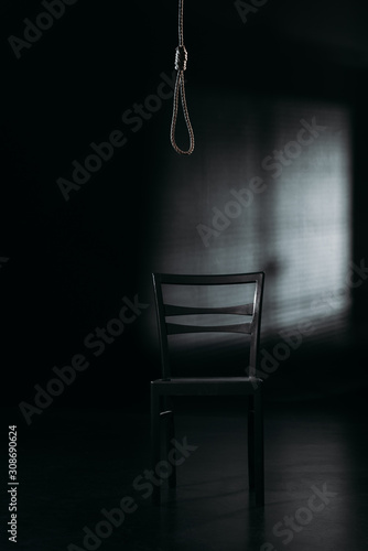 chair under hanging rope noose on black background with lighting, suicide prevention concept