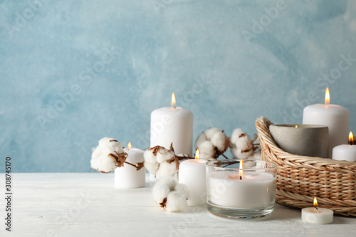 Burning candles, basket and cotton on white wooden table, space for text