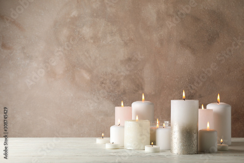 Burning candles on white wooden table against brown background, space for text
