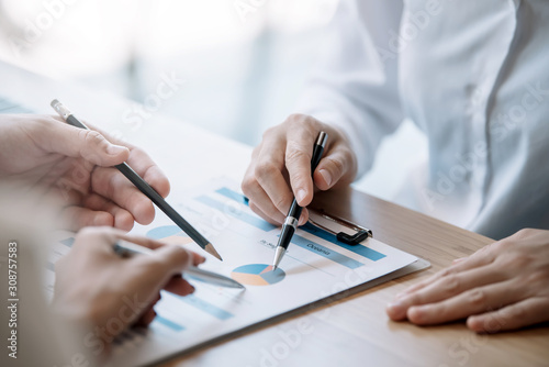 Business people gather to analyze marketing and investment information and using pen pointing to financial data chart at meeting.