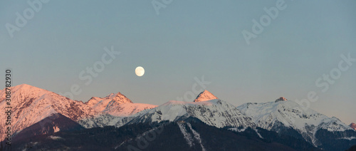 Amazing sunset and full moon over Caucasus mountains covered by snow in Krasnaya Polyana, Russia.