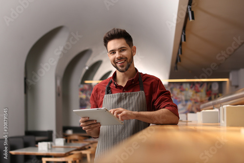 Young male business owner with tablet near counter in his cafe