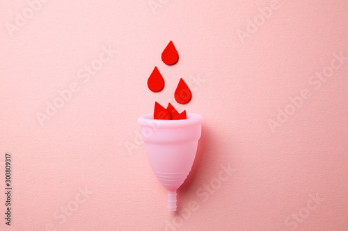 Silicone menstrual cup. Women's health and alternative hygiene. Cup with drops of blood on a pink background.