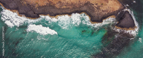 Aerial view of aqua sea waves breaking on rocky cliff, adventure summer travel vacation, perseverance and resilience concept, decarbonisation concept