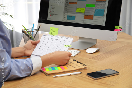 Woman making schedule using calendar at table in office, closeup