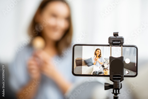 Young woman recording on a smart phone her vlog about cosmetics, showing and demonstrating makeup, close-up on phone. Influencer marketing in social media concept