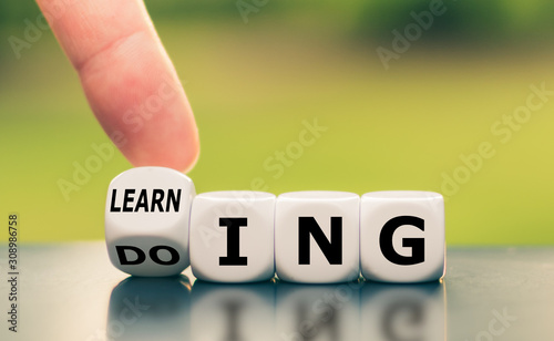 Learning by doing concept. Hand turns a dice and changes the word "learning" to "doing", or vice versa.