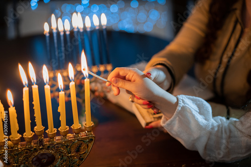 jewish holiday Chanukah/Hanukkah family selebration. Jewish festival of lights. Children lighting candles on traditional menorah over glitter shiny background