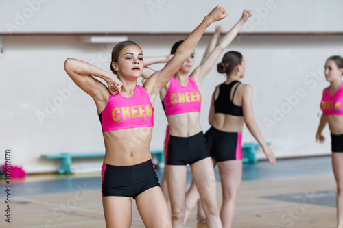 cheerleaders train at the gym, smiling beautiful girl in black and pink sportswear showing strength and power, sport young women with perfect body raise their hand up