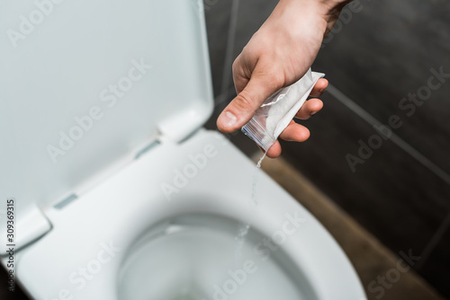 cropped view of man pouring out cocaine in toilet bowl in modern restroom with grey tile