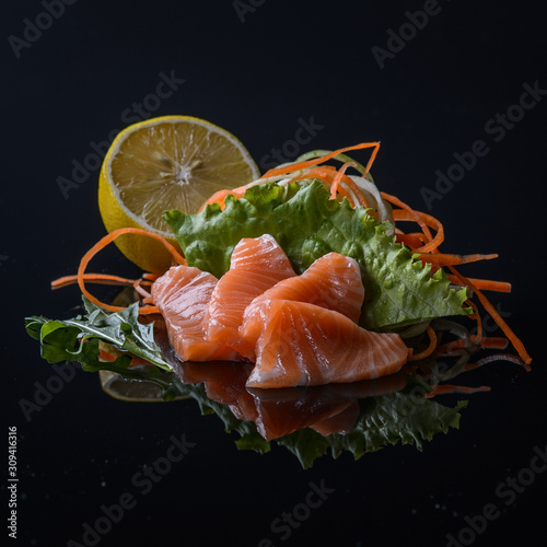 salmon's sashimi with salad and lemon on black background