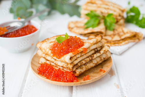 Classic thin lace pancakes on a wooden plate with red caviar on a light background. A traditional dish for Shrove Tuesday