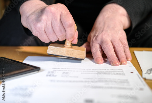 Konzept Büroarbeit: Ältere Frau bearbeitet und beglaubigt ein Schriftstück mit einem abgenutzten Stempel - selektive SchÃ¤rfe, Copyspace