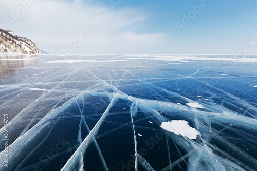 The endless ice desert of the frozen Baikal Lake. Snow-covered hills on the shore and thick blue ice with cracks to the horizon. Ice travel. Winter cold background