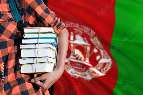 Afghanistan national education concept. Close up of teenage student holding books under his arm with country flag background.