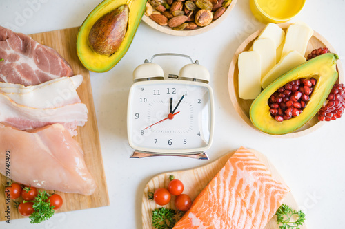 Intermittent fasting and Healthy food. Concept.Alarm clock and Keto diet food ingredients on white table.Ketogenic mean Low carb and High fat.