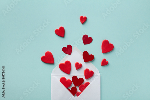 Valentine day greeting concept. Envelope and red hearts on blue background top view. Flat lay.