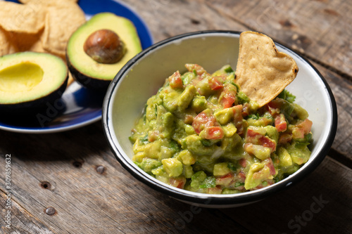 Mexican guacamole with tomato on wooden background