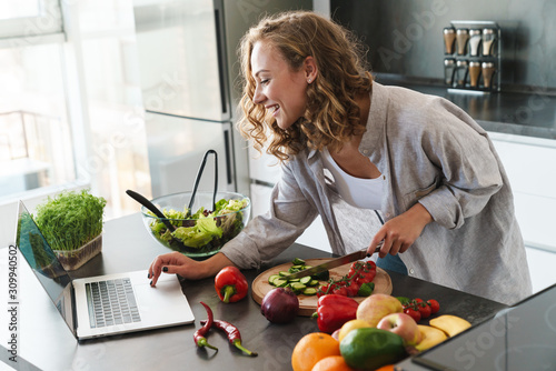 Happy young woman making a salad at the kitchen