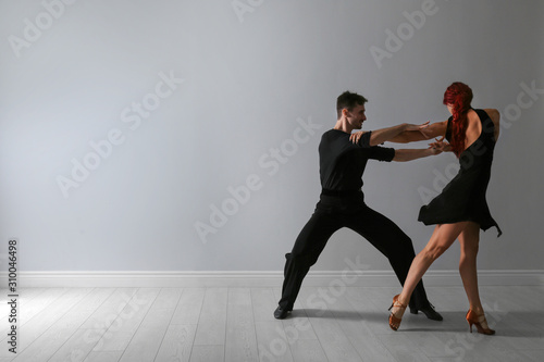 Beautiful young couple dancing near light wall. Space for text