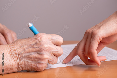 Woman of retirement age signs a document. Elderly woman signs a paper document. Signing papers. An elderly man signs a document.