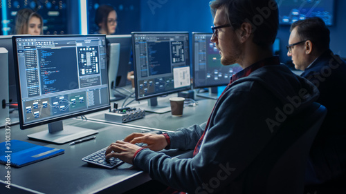 Smart Male IT Programer Working on Desktop Green Mock-up Screen Computer in Data Center System Control Room. Team of Young Professionals Programming Sophisticated Code