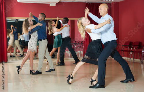 Positive adult couples dancing tango together in modern studio