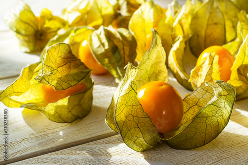 Many yellow ripe physalis fruits (Physalis peruviana) in the sunshine on a white wooden table. Fruits and vegetables, vegetarian and healthy eating. Ready to eat.