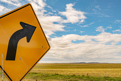 Yellow right turn signal, a black arrow with a green field in the background and a blue sky with clouds. Way to heaven