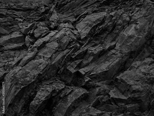 Black white rock background. Dark gray stone texture. Mountain surface close-up. Distressed, сracked, collapsed, crumbled, broken. 