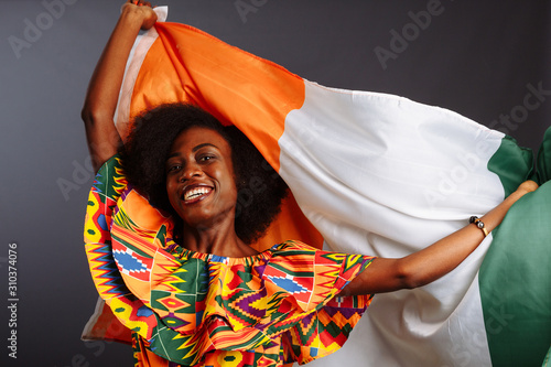 Happy african woman in national clothes smiling and posing with a flag Ivory Coast, C te d'Ivoire isolated over a gray background