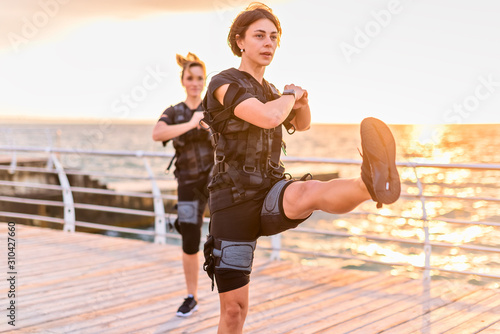 Women with her instructor training in EMS trainer on seaside at sunrise
