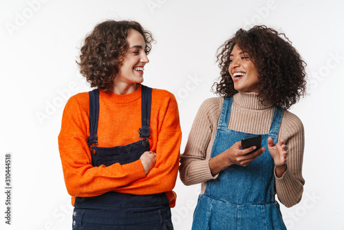 Portrait of joyful multinational women laughing and using cellphone