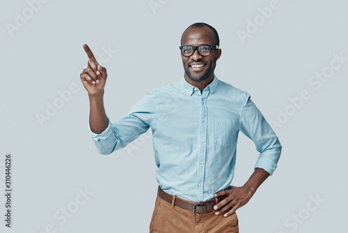 Charming young African man pointing copy space and smiling while standing against grey background