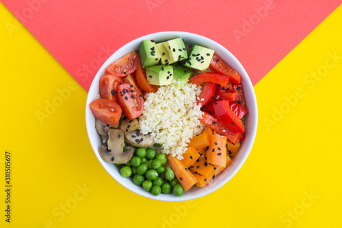 Vegan poke bowl with couscous and vegetables in the white bowl in the center of the bicolor background. Top view. Copy space. Closeup.