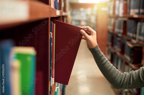 Asia female Hand picking book from bookshelf at library university,a concept of learning and choice