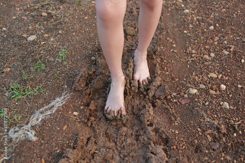 Kid bare foot with muddy feet on the rural road.