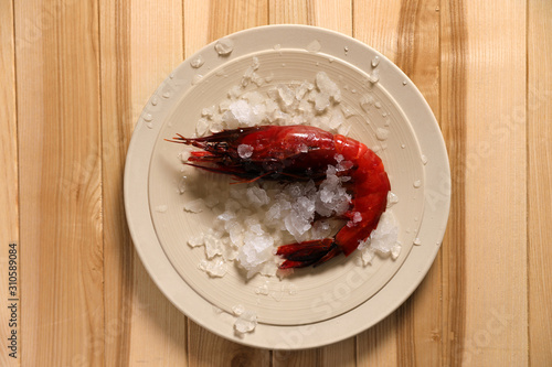 Fresh carabinero shrimp with ice on wooden table, top view