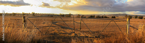 Panoramic views of dry, drought stricken farm land through old steel locked farm gates on a hot afternoon in Gunnedah, New South Wales, rural Australia